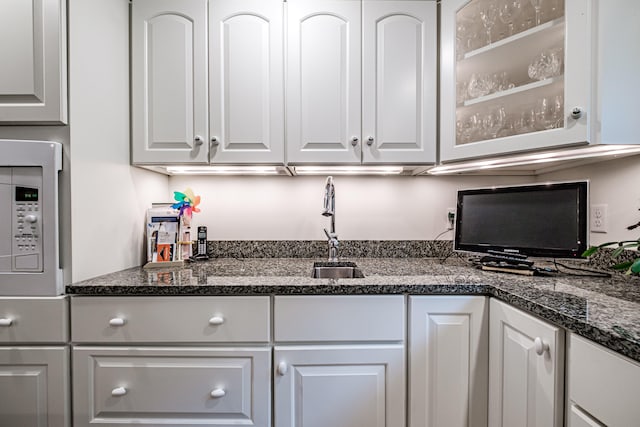 kitchen with white microwave, white cabinetry, and dark stone countertops