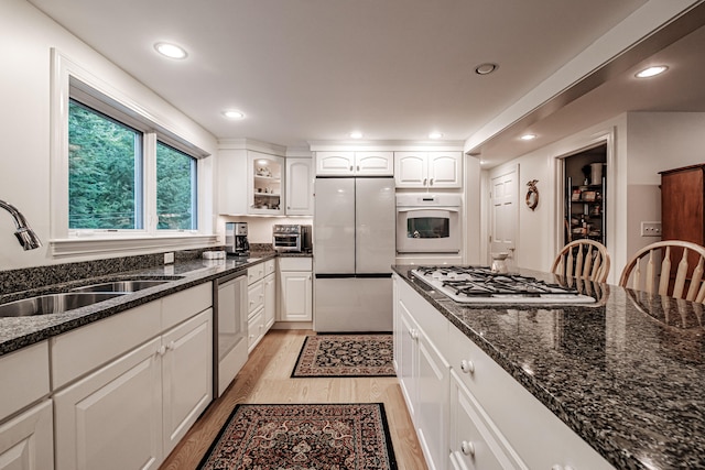 kitchen featuring white cabinetry, light wood-type flooring, dark stone counters, appliances with stainless steel finishes, and sink