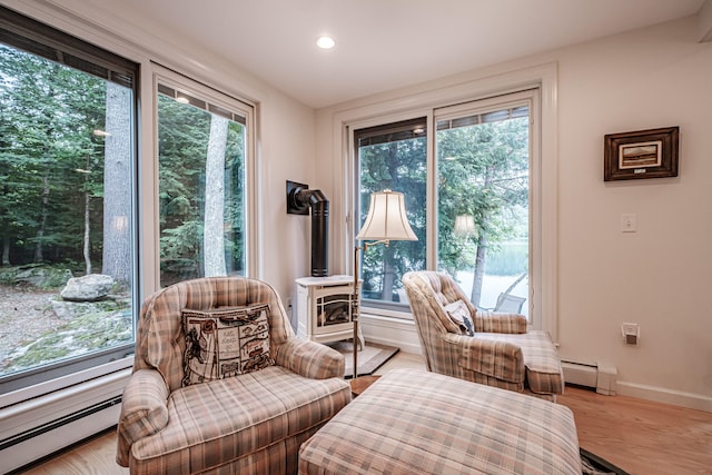 sitting room with a wood stove, light hardwood / wood-style flooring, and a baseboard radiator