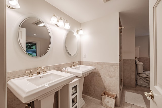 bathroom featuring tile patterned flooring, tile walls, toilet, and sink