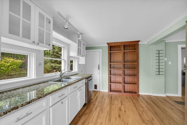 kitchen with dark stone countertops, white cabinets, light hardwood / wood-style flooring, and sink