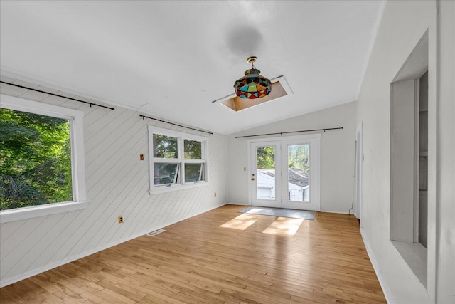 spare room featuring light wood-type flooring, wood walls, vaulted ceiling, and french doors