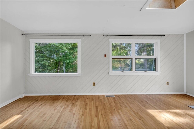 empty room with a wealth of natural light, light wood-type flooring, and wooden walls