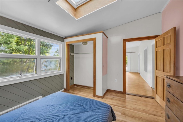 bedroom with light wood-type flooring, wooden walls, a skylight, and a closet