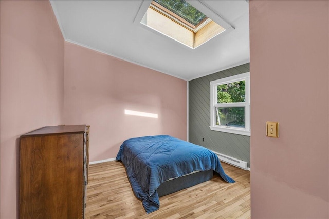 bedroom with vaulted ceiling with skylight, ornamental molding, wooden walls, a baseboard heating unit, and light hardwood / wood-style floors