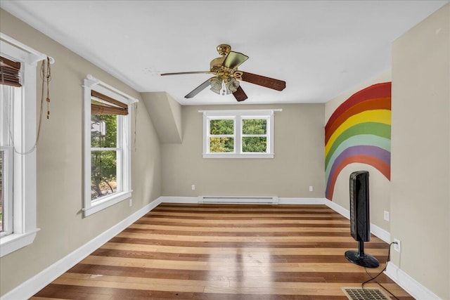 unfurnished living room featuring a wealth of natural light, ceiling fan, baseboard heating, and light wood-type flooring