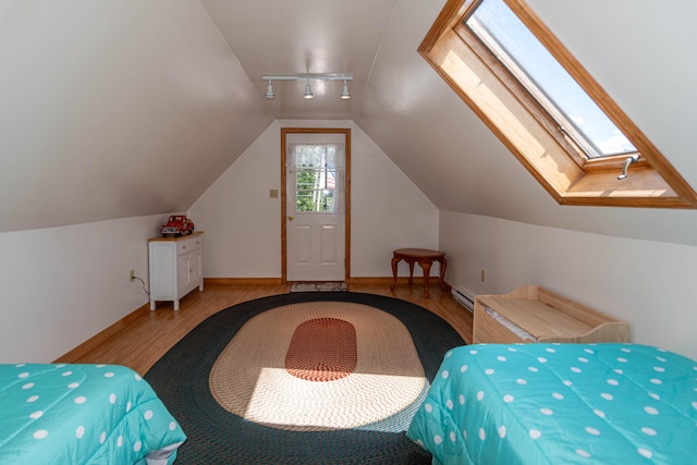 803 Lake Shore Rd, Madawaska, ME 04773 - bedroom featuring wood finished floors, a baseboard radiator, rail lighting, baseboards, and lofted ceiling with skylight