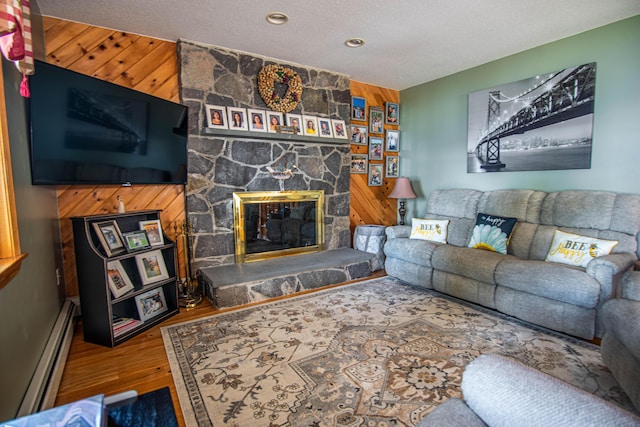 803 Lake Shore Rd, Madawaska, ME 04773 - living area with wood finished floors, wood walls, a textured ceiling, a stone fireplace, and a baseboard radiator