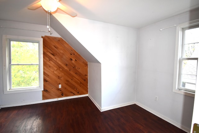 bonus room with dark wood-type flooring, wood walls, and ceiling fan