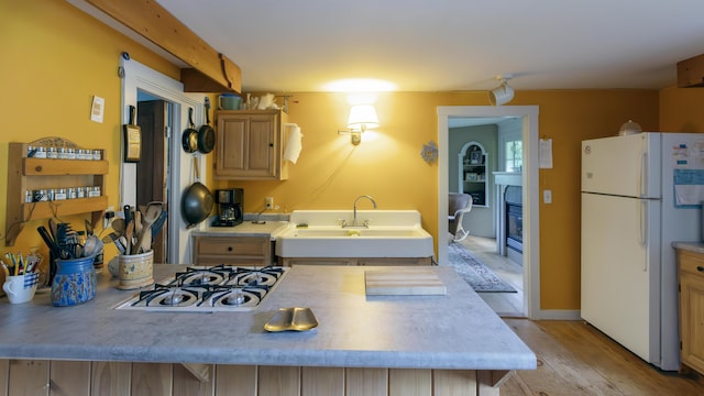 kitchen with gas stovetop, freestanding refrigerator, a glass covered fireplace, light brown cabinets, and a sink