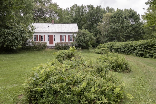 view of front of home featuring metal roof, a chimney, and a front lawn