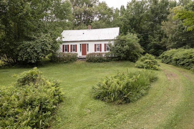 view of front of property featuring metal roof, a front lawn, and a chimney