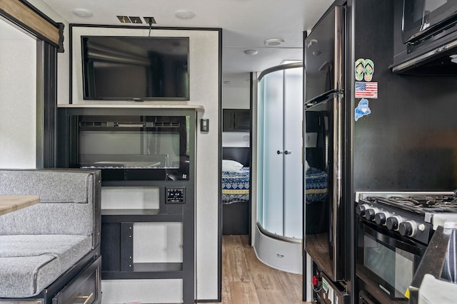 kitchen with black appliances, stone counters, and light hardwood / wood-style flooring