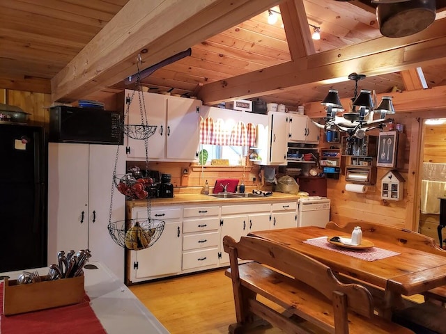 kitchen with black appliances, beam ceiling, white cabinets, and wooden walls