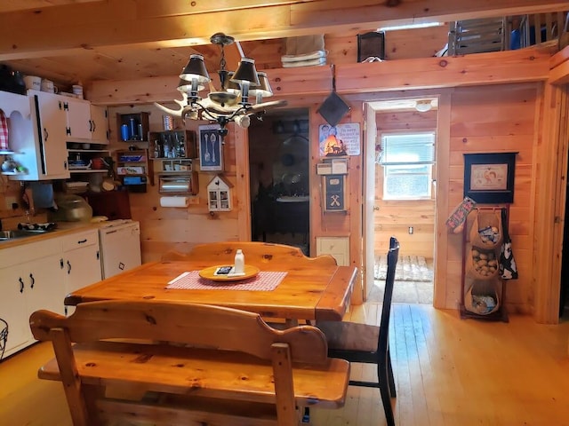 dining area with wood walls, a chandelier, and light hardwood / wood-style floors