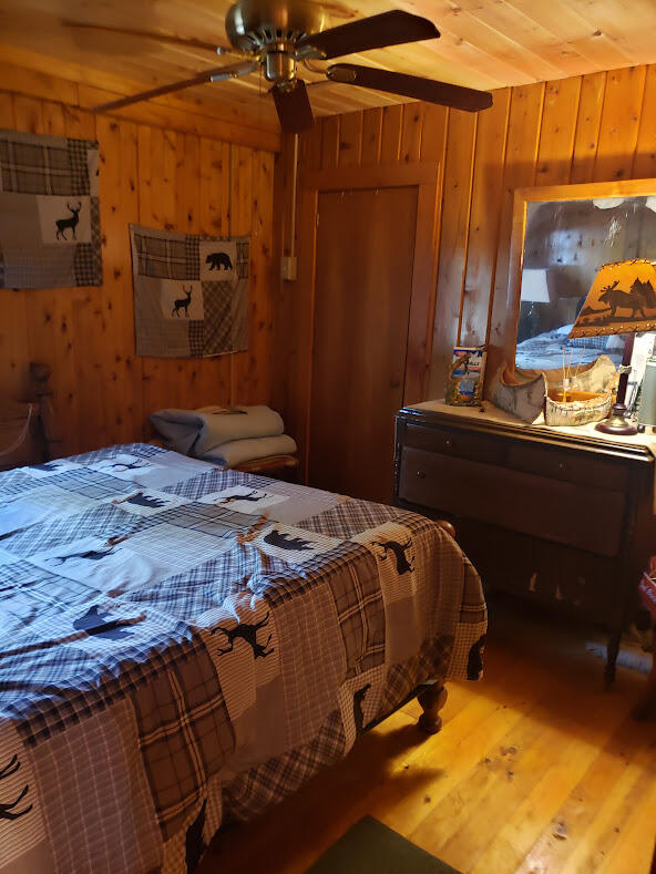 bedroom featuring wood-type flooring, wood ceiling, wooden walls, and ceiling fan