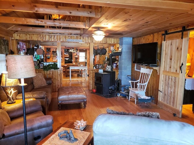 living room with a wood stove, hardwood / wood-style floors, a barn door, beam ceiling, and wood walls