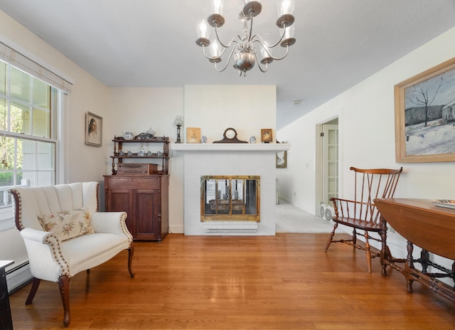 living area with baseboard heating, light hardwood / wood-style flooring, a fireplace, and an inviting chandelier