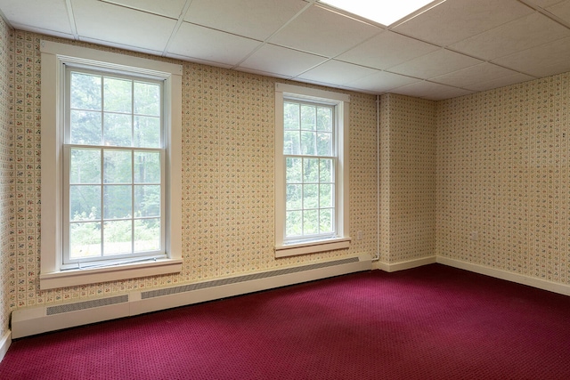 empty room featuring a drop ceiling, a baseboard radiator, and carpet floors