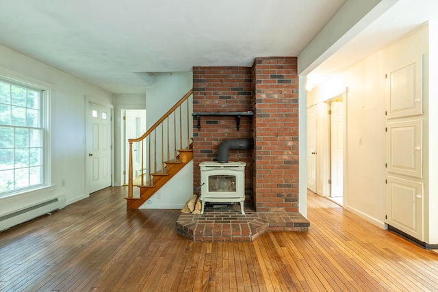 unfurnished living room with a wood stove, brick wall, hardwood / wood-style flooring, and plenty of natural light