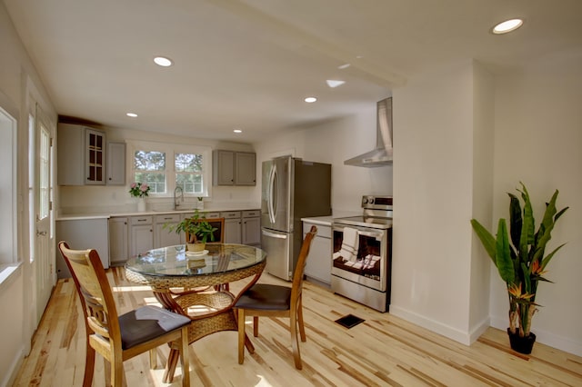 kitchen featuring appliances with stainless steel finishes, light countertops, glass insert cabinets, and wall chimney exhaust hood