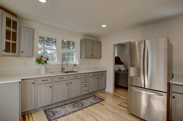 kitchen with a sink, light countertops, stainless steel refrigerator with ice dispenser, light wood finished floors, and glass insert cabinets