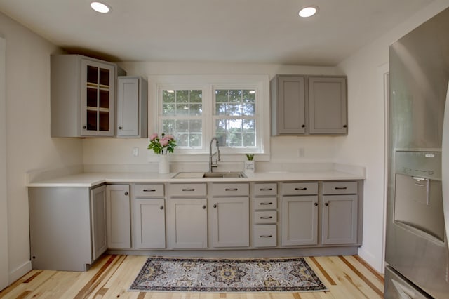 kitchen featuring light countertops, gray cabinetry, glass insert cabinets, a sink, and stainless steel fridge with ice dispenser