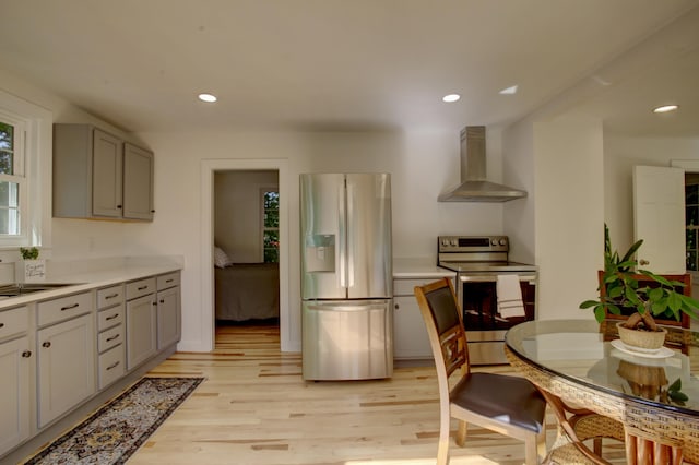 kitchen with gray cabinetry, stainless steel appliances, light wood-style floors, light countertops, and wall chimney exhaust hood