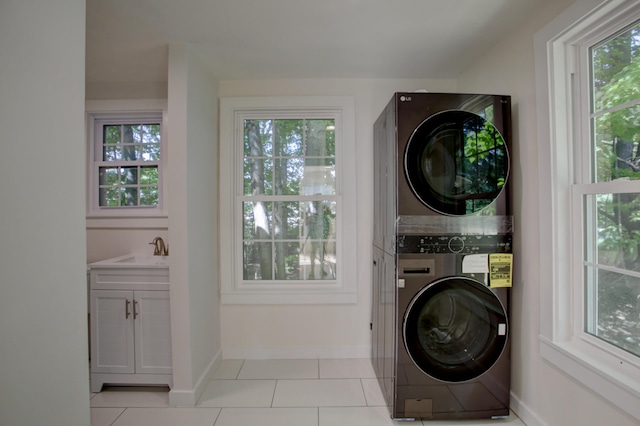 laundry area featuring light tile patterned floors, laundry area, a sink, baseboards, and stacked washer and clothes dryer