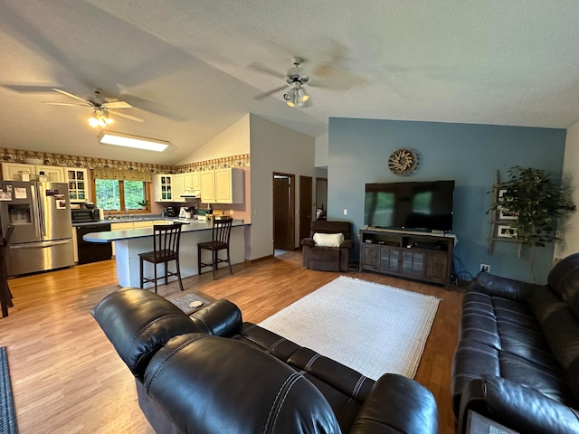 living room featuring ceiling fan, vaulted ceiling, a textured ceiling, and light hardwood / wood-style floors