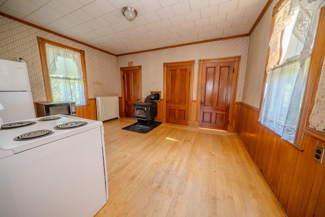 kitchen featuring radiator, light hardwood / wood-style floors, a wood stove, ornamental molding, and white appliances