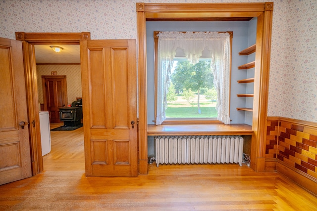 empty room featuring a wood stove, light wood-type flooring, and radiator heating unit