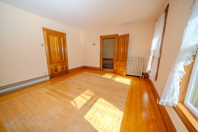 spare room featuring radiator heating unit, light wood-type flooring, and a baseboard heating unit