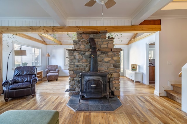 living room featuring beam ceiling, ceiling fan, light hardwood / wood-style floors, and a wood stove