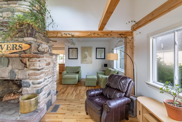 living area featuring beamed ceiling, a stone fireplace, light wood-type flooring, and a wealth of natural light