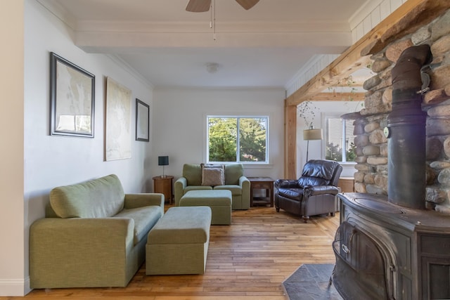 living room with ceiling fan, ornamental molding, a wood stove, and light wood finished floors