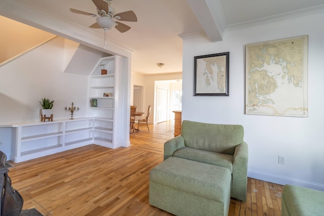 living area with built in shelves, beam ceiling, wood-type flooring, baseboards, and ceiling fan