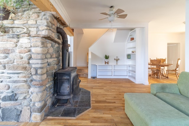 living room featuring ceiling fan, a wood stove, light hardwood / wood-style flooring, and ornamental molding