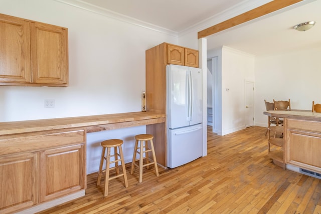 kitchen with visible vents, freestanding refrigerator, ornamental molding, a kitchen bar, and light wood-type flooring