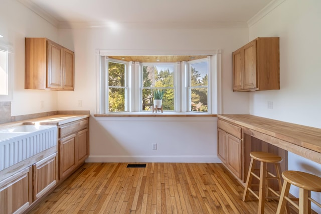 kitchen featuring visible vents, baseboards, crown molding, and light wood-style floors