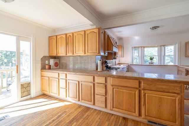 kitchen with tile countertops, backsplash, ornamental molding, light hardwood / wood-style floors, and kitchen peninsula