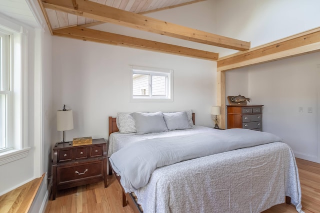 bedroom featuring lofted ceiling with beams, baseboards, and light wood-style floors