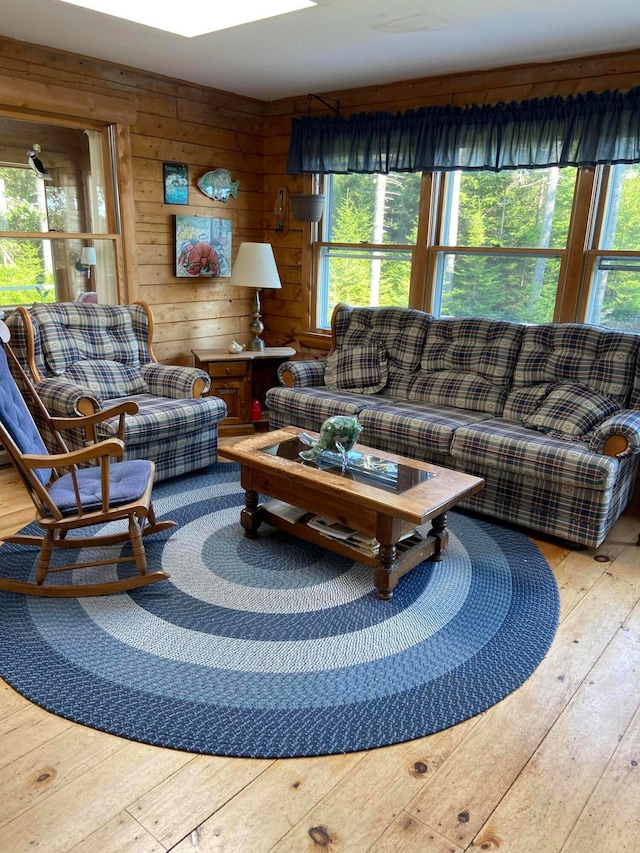 living room with light hardwood / wood-style flooring, wooden walls, and a healthy amount of sunlight