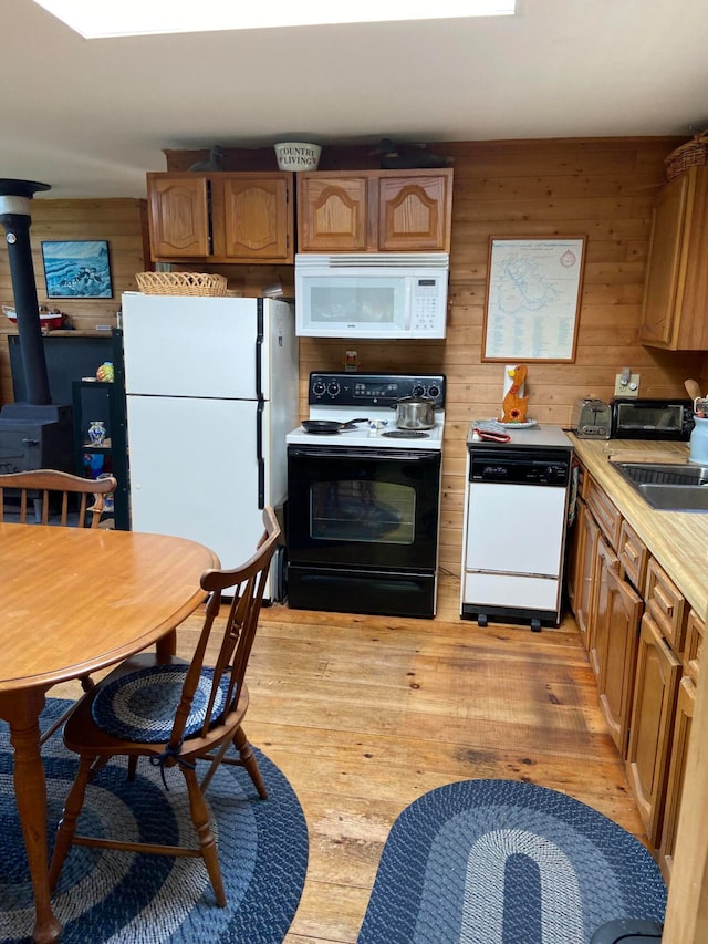 kitchen featuring white appliances, light wood-type flooring, sink, wood walls, and a wood stove