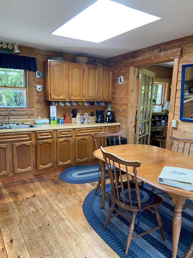 kitchen featuring wood walls, sink, light hardwood / wood-style floors, and a skylight