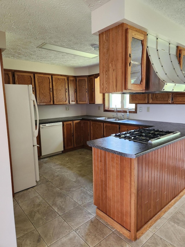 kitchen featuring a textured ceiling, kitchen peninsula, light tile patterned floors, white appliances, and sink