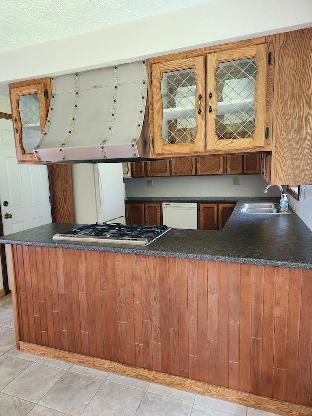 kitchen with white appliances, brown cabinetry, a sink, dark countertops, and exhaust hood