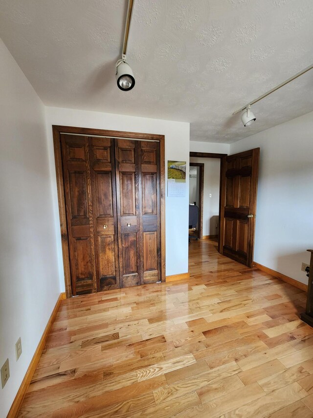 unfurnished bedroom featuring light hardwood / wood-style flooring, a textured ceiling, and rail lighting