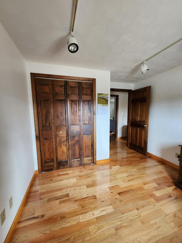 unfurnished bedroom featuring a textured ceiling, light wood-type flooring, and baseboards