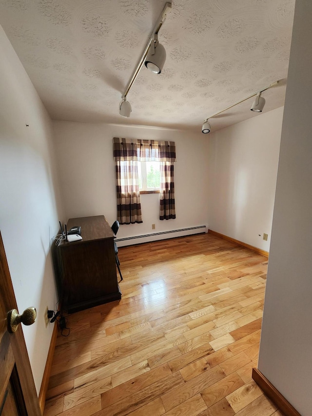 unfurnished room with light wood-style flooring, track lighting, a textured ceiling, a baseboard radiator, and baseboards